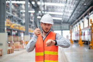A confident male engineer stands with arms crossed in a large train maintenance hall
