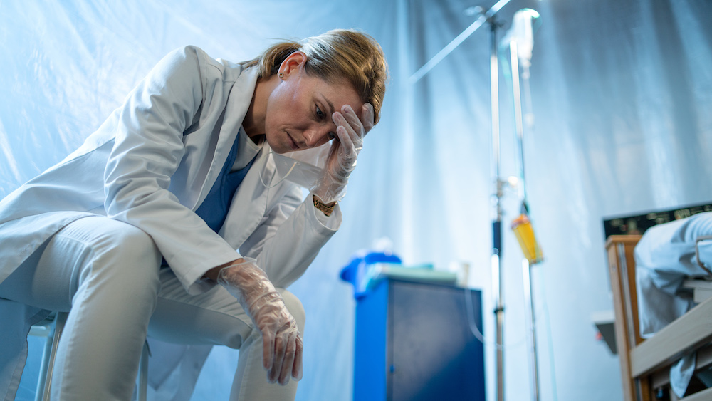 Tired and frustrated doctor sitting by patient in bed